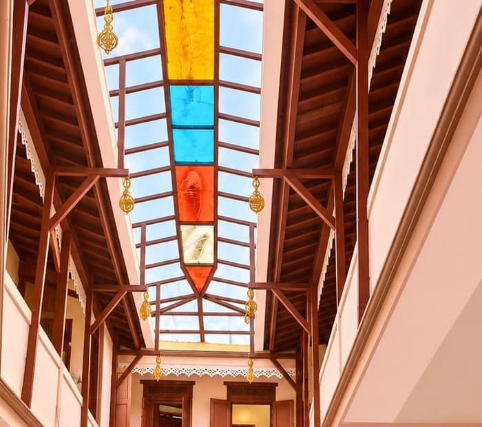 Coloured-glass skylight above the courtyard framed by carved wooden galleries and hanging bells